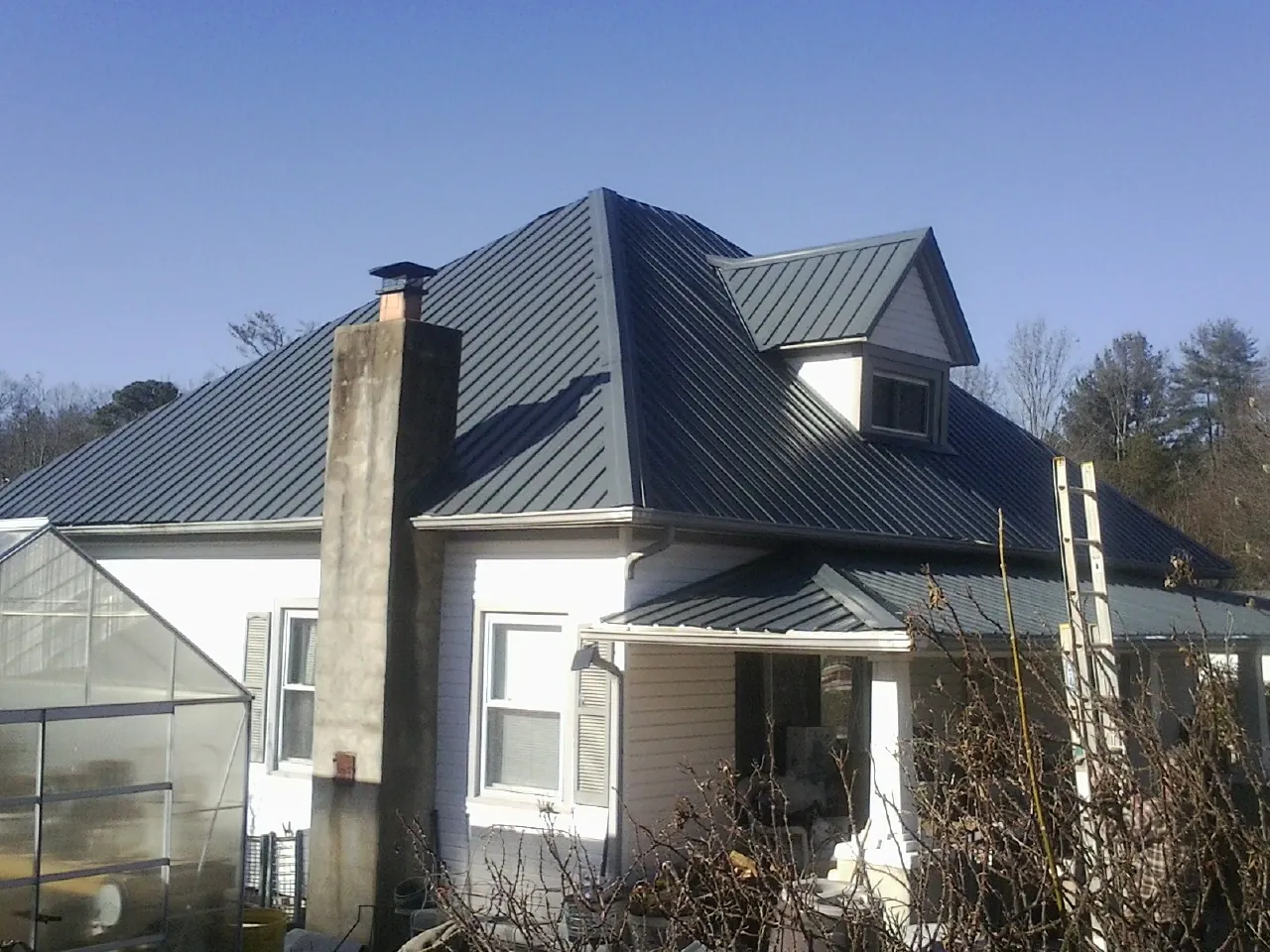 Dark blue standing seam metal roof on a white farmhouse with dormer — Slate & Tile Roof Repair by Roofing Brothers in Big Timber