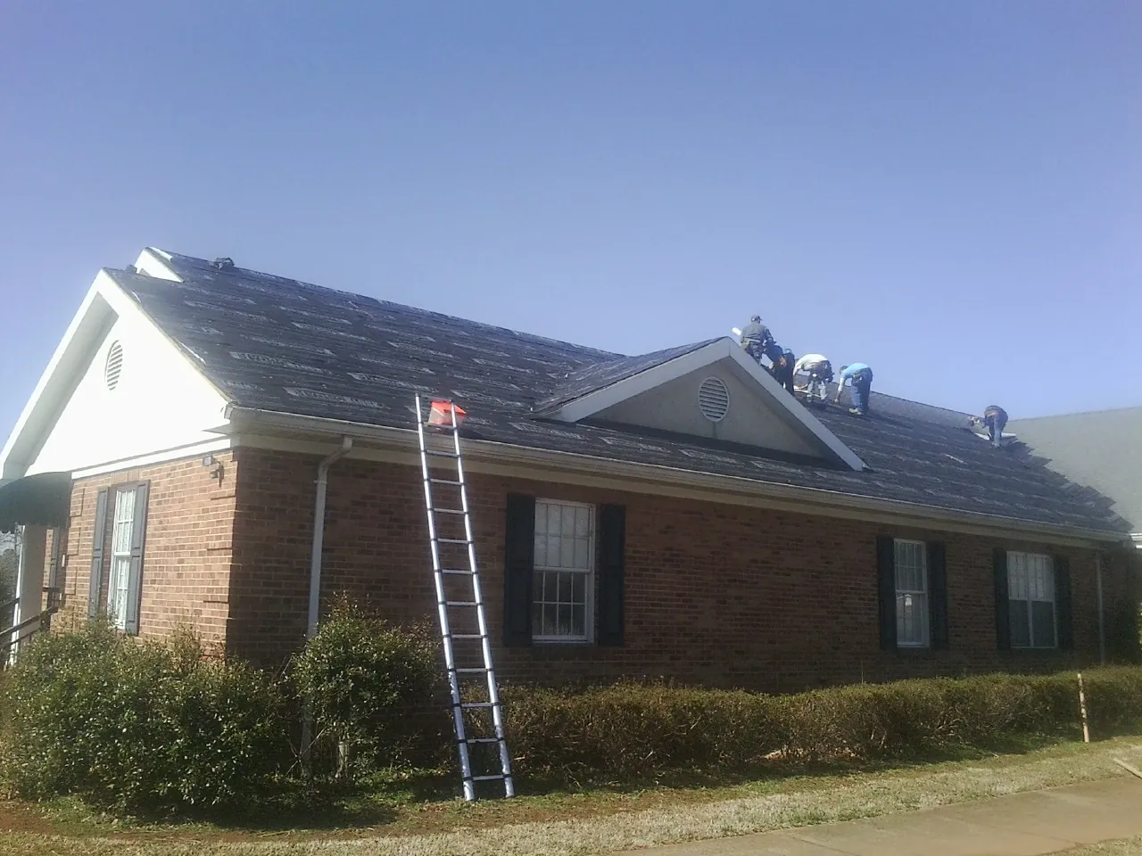 Crew tearing shingles off a brick ranch roof with a ladder set — Emergency Roof Repair work by our crew in Big Timber