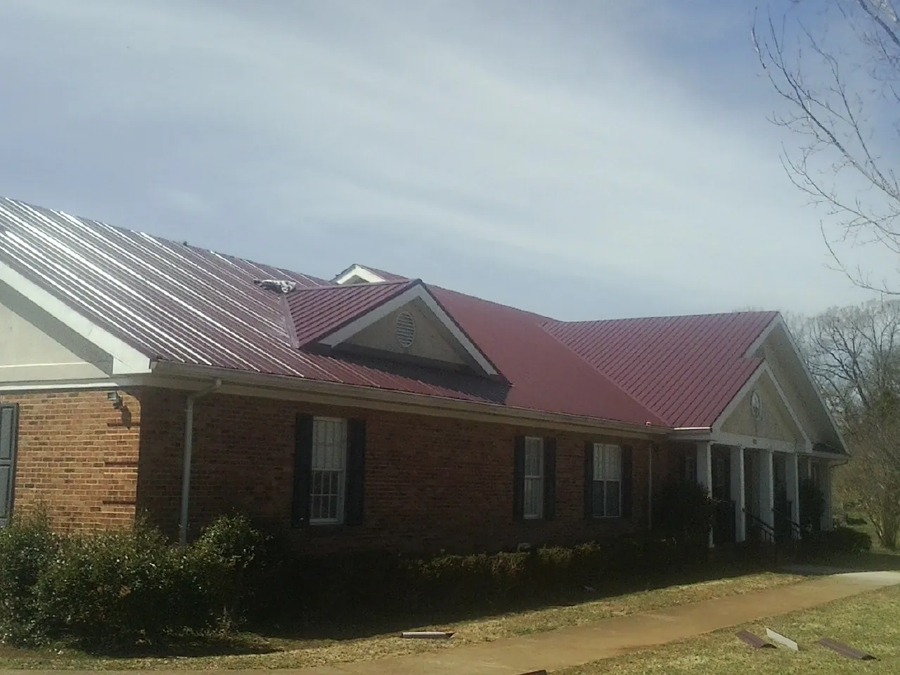 Red metal roof with gabled entries on a long brick building, from a Hail Damage Roof Repair job in Big Timber