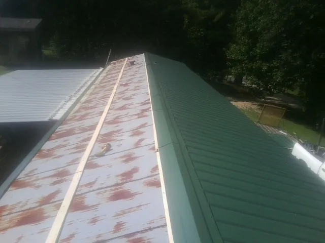 Old rusted panels beside newly installed green metal roofing — Wind Damage Roof Repair by Roofing Brothers in Big Timber