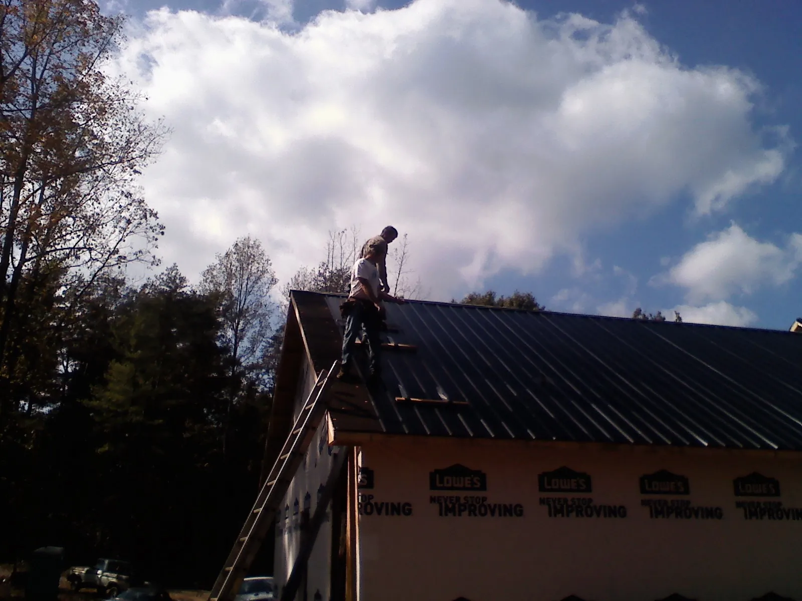Roofer fastening dark metal panels high against a cloudy sky, from a Roof Inspection job in Big Timber
